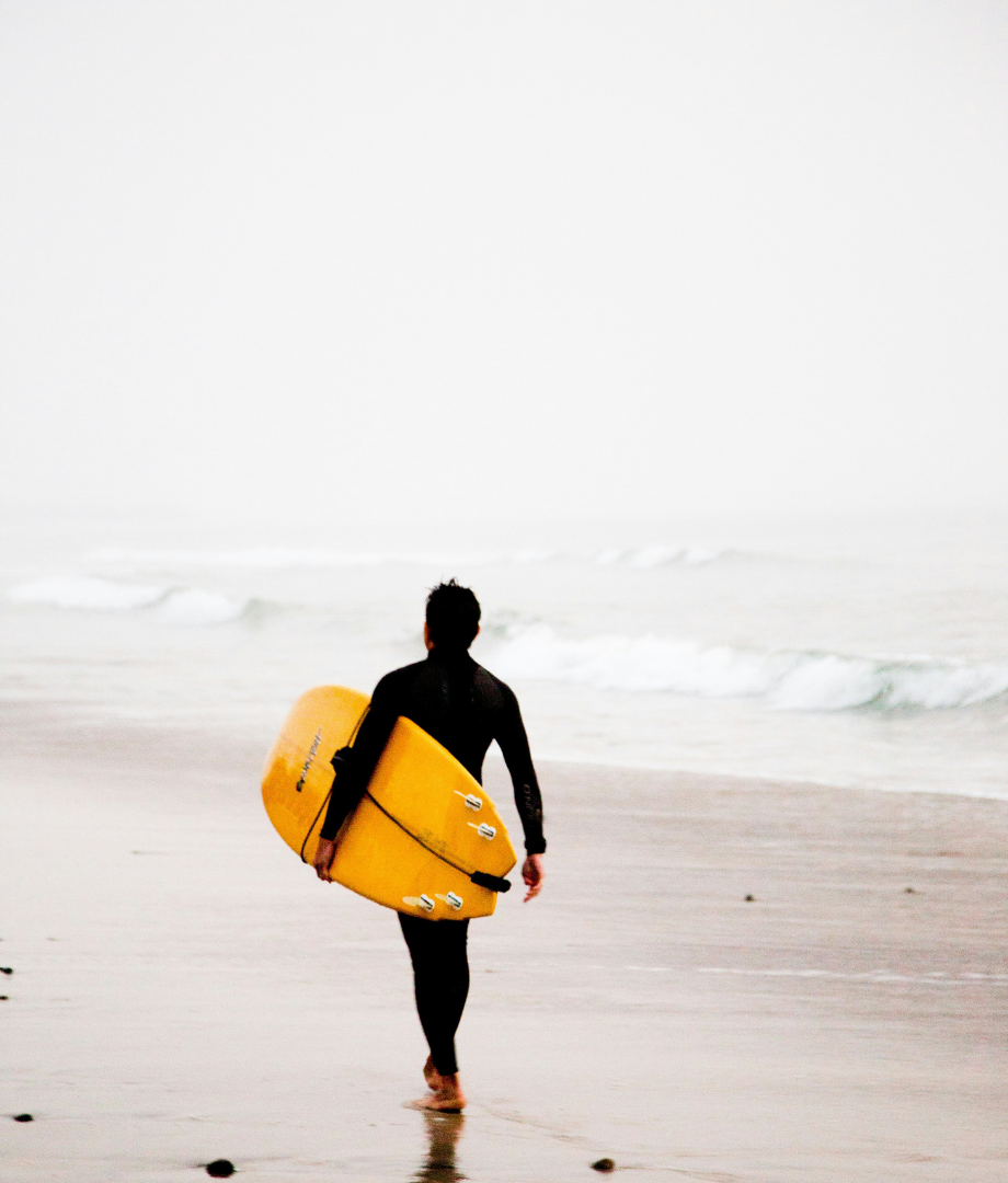 Surfer walking on a sunny beach protected with the best sunscreen for outdoor sports.