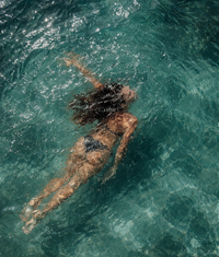 Person swimming in clear blue water protected by reef safe sun care.