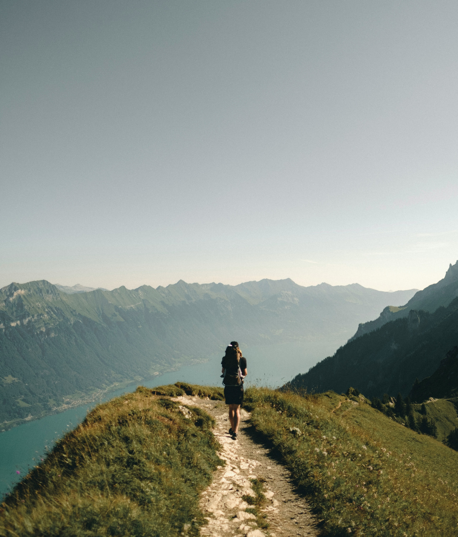 Person hiking with mountain and lake views, using aloe vera mist.
